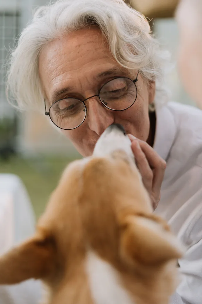 An elderly woman smiling with a dog on her lap